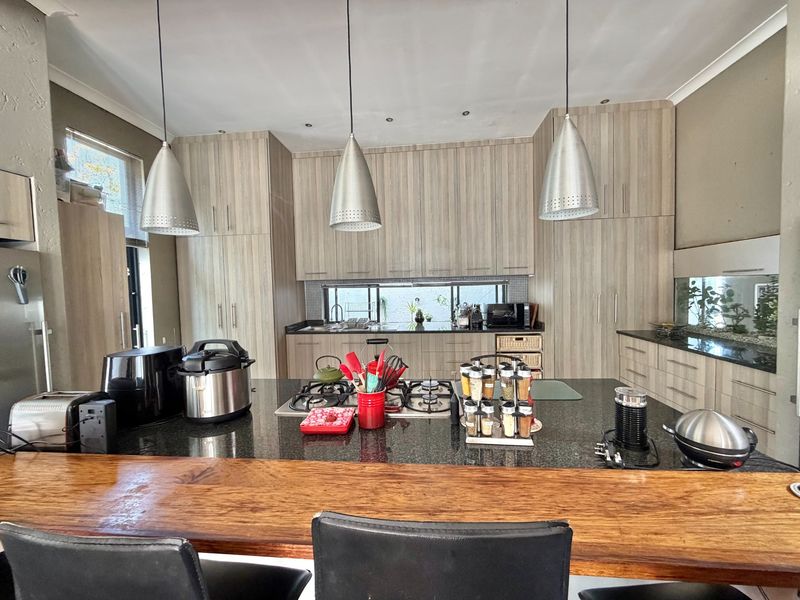Modern kitchen featuring extensive light wood cabinetry, granite countertops, a central island with a gas hob, and stylish pendant lighting.