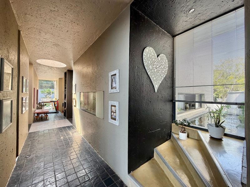 A spacious hallway featuring textured walls, tiled flooring, a skylight, and a staircase leading to a windowed area with natural light.
