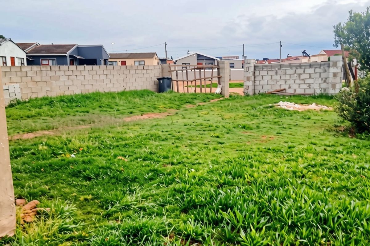 A spacious rear yard featuring a grass lawn and partially completed concrete block boundary walls with gated access.