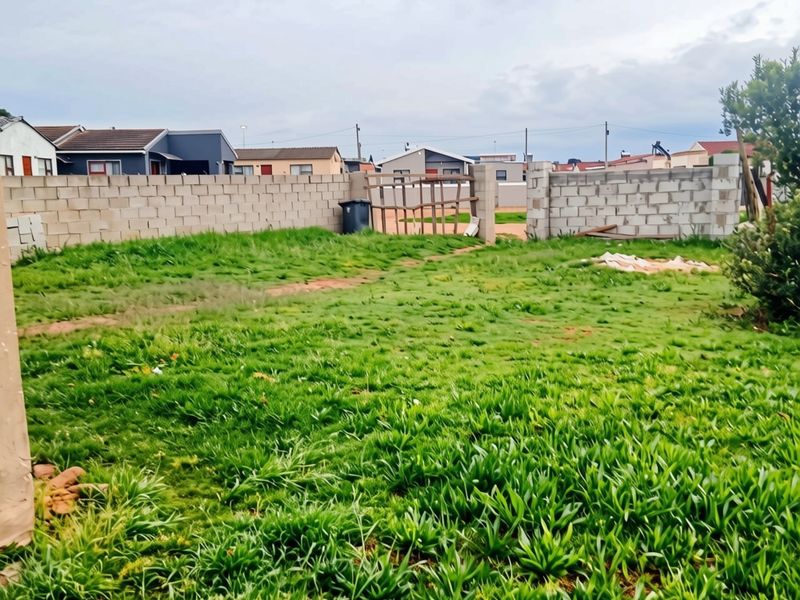 A spacious rear yard featuring a grass lawn and partially completed concrete block boundary walls with gated access.