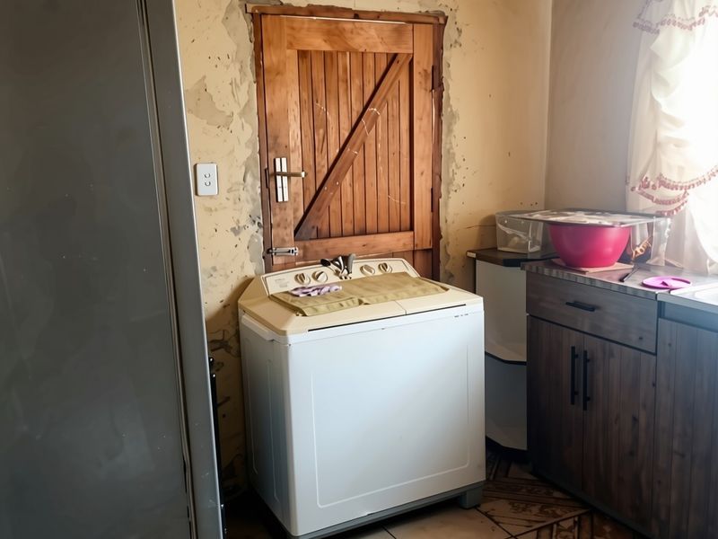 A laundry area featuring timber ceiling, tiled floors, and built-in cabinetry, currently requiring wall repairs and cosmetic updates to improve the space.