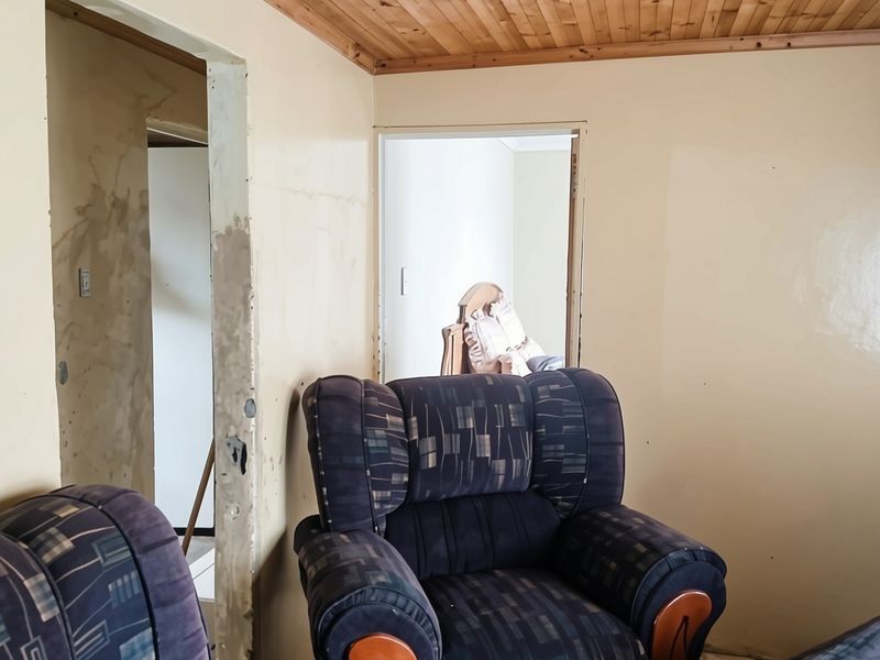 Living room featuring a timber ceiling and tiled flooring, currently requiring wall repairs and finishing to improve the overall condition.