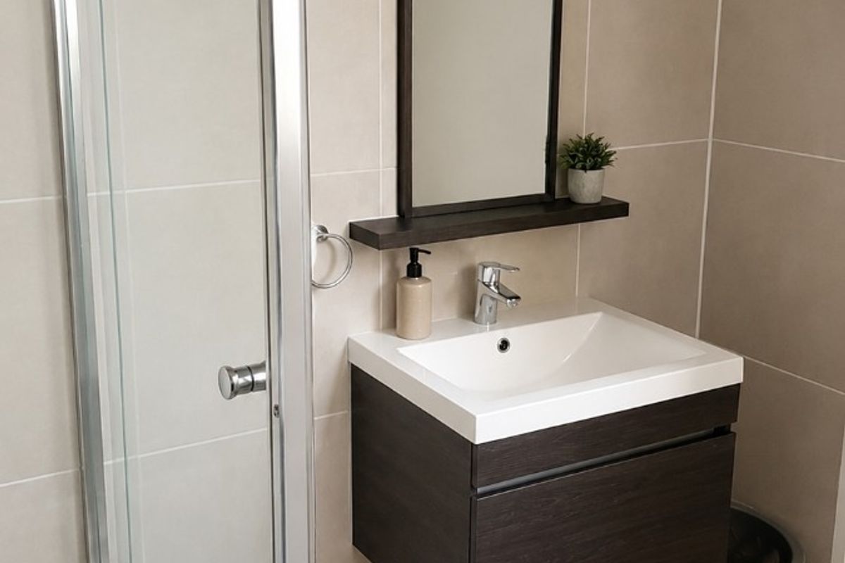 A modern bathroom featuring a wall-mounted vanity with an integrated basin, a framed mirror, and a glass-enclosed shower with neutral wall and floor tiling.