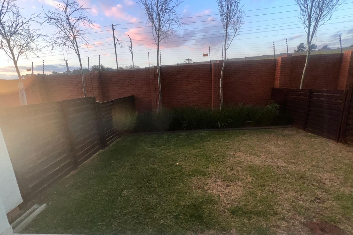 A private rear garden featuring a tiled patio area, lawn, and secure brick boundary wall with electric fencing.