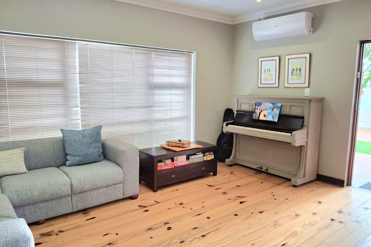 A bright living room featuring polished timber flooring, a wall-mounted split-system air conditioner, and large windows fitted with venetian blinds.