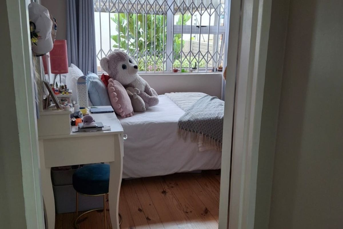 A cozy bedroom featuring polished timber flooring, a wall-mounted air conditioning unit, and a window fitted with a security gate.