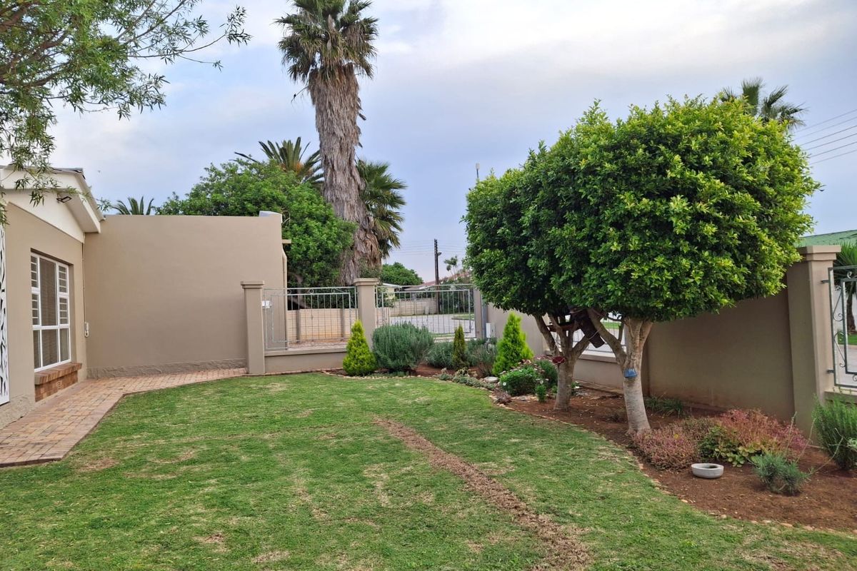A well-maintained rear garden featuring a manicured lawn, paved walkway, and established boundary walls with secure metal gate access.