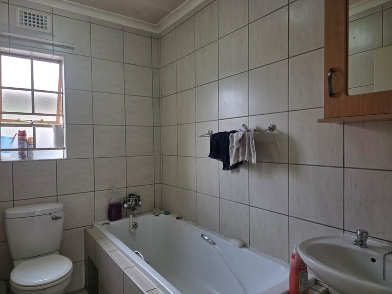 A functional bathroom featuring a bathtub, pedestal basin, toilet, and full-height wall tiling, providing a practical layout with natural light.