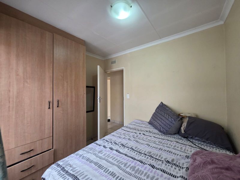 A functional bedroom featuring a built-in wooden wardrobe and neutral wall finishes, providing a practical and comfortable sleeping space.