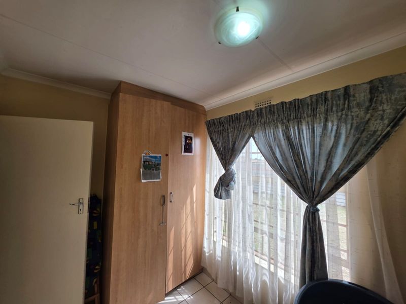 A bedroom featuring tiled flooring, a built-in wooden wardrobe, and a window with curtains.