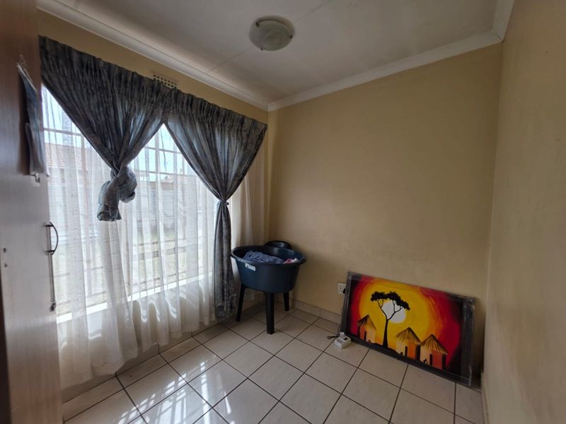 A simple, empty bedroom featuring tiled flooring and a window with security bars, offering a blank canvas for potential interior updates.