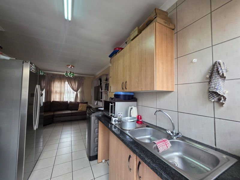 Open plan kitchen and living area featuring tiled flooring, laminate cabinetry, and a double bowl stainless steel sink with a tiled splashback.
