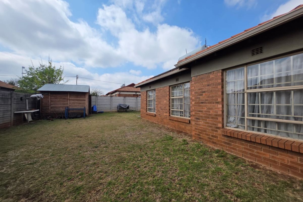 Rear view of the property featuring a brick facade, metal roofing, a solar geyser, and a spacious backyard with a timber garden shed.