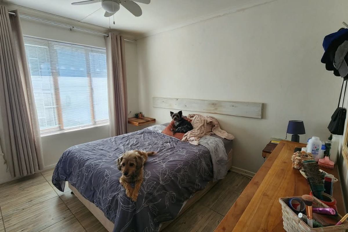 A bedroom featuring tiled flooring, a ceiling fan, and a large window with curtain tracks.