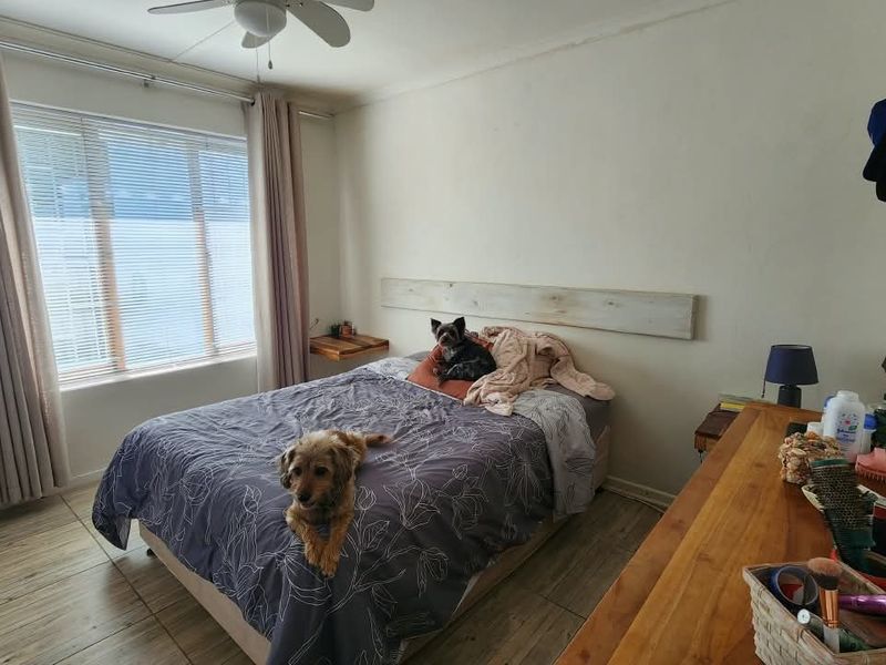 A bedroom featuring tiled flooring, a ceiling fan, and a large window with curtain tracks.