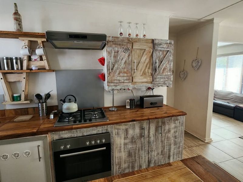 A rustic-style kitchen featuring wooden countertops, built-in gas hob, oven, extractor fan, and custom cabinetry, flowing into an adjacent living area with tiled floors.