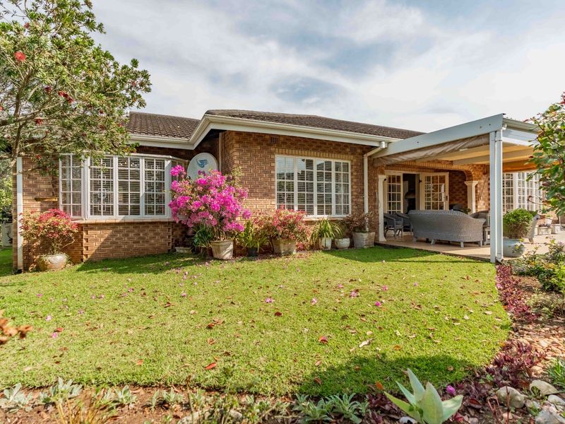 Rear view of the townhouse featuring a brick facade, a covered patio area, and a well-maintained garden with established landscaping.