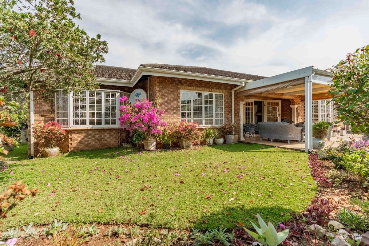 Rear view of the townhouse featuring a brick facade, a covered patio area, and a well-maintained garden with established landscaping.