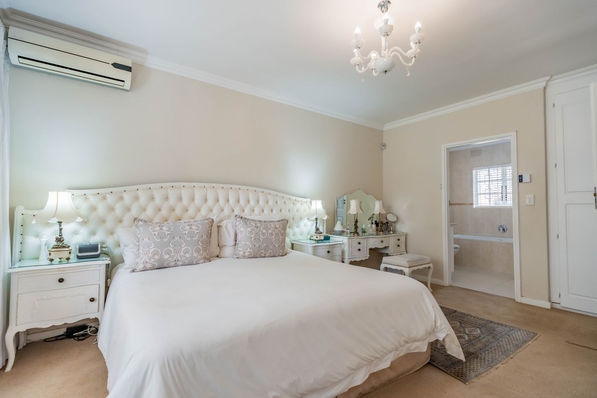 Spacious bedroom featuring neutral tones, carpeted flooring, a split-system air conditioner, and direct access to an en-suite bathroom.