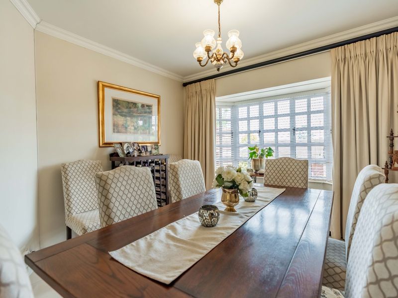 A well-maintained dining room featuring a classic bay window, elegant crown molding, and a central chandelier, creating a warm and inviting atmosphere.