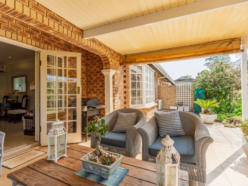 A covered brick patio featuring tiled flooring, a retractable awning, and direct access to the interior through classic french doors.