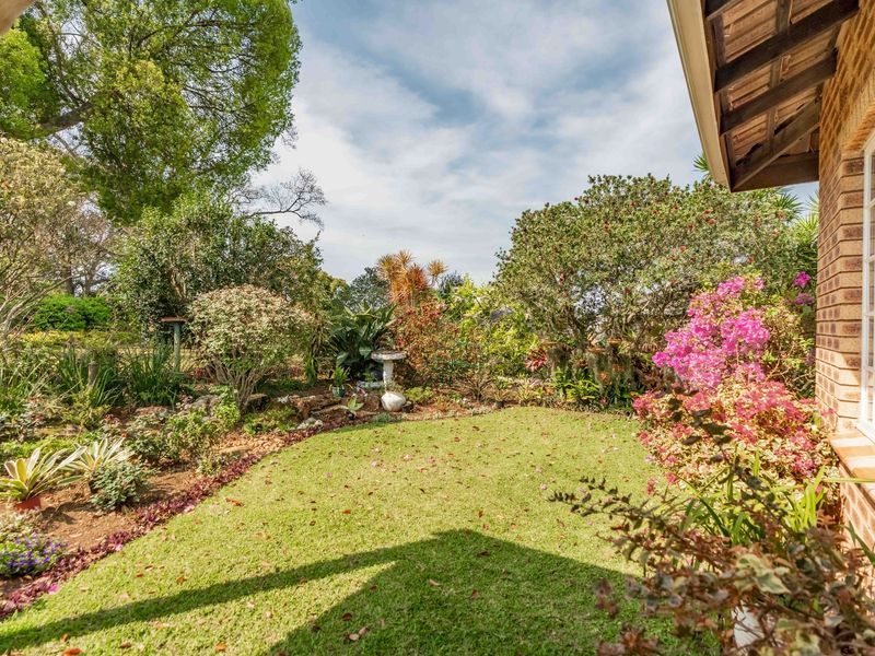 A well-maintained private garden featuring lush landscaping, mature trees, and a brick exterior facade with classic multi-pane windows.