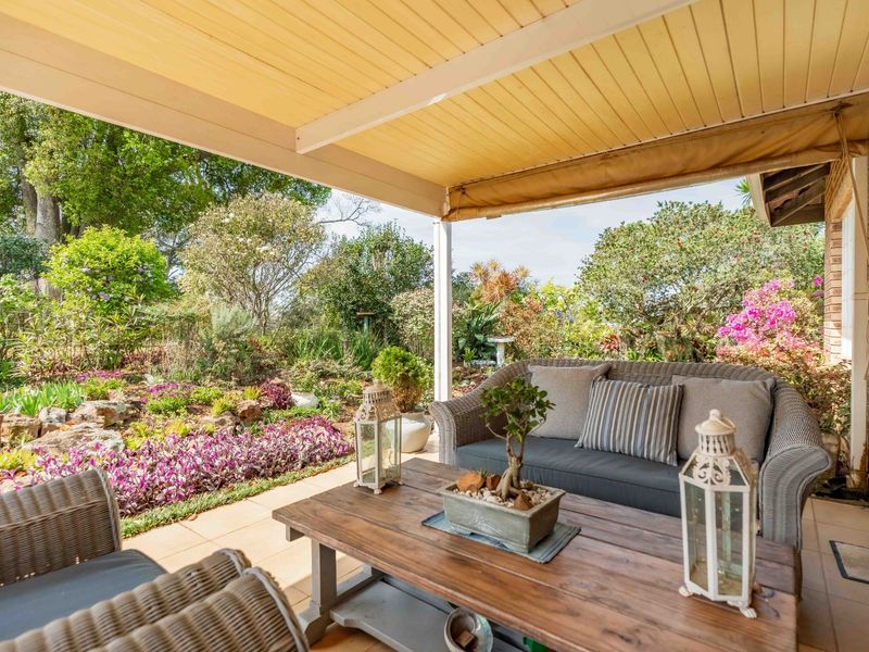 A well-maintained covered patio featuring tiled flooring and a timber ceiling, overlooking a lush, landscaped garden.
