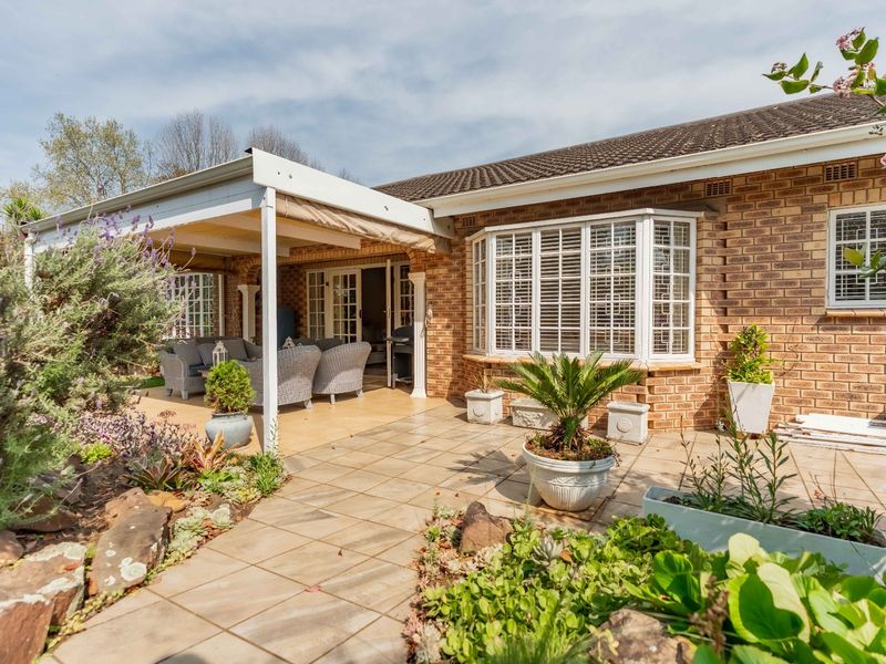 A well-maintained rear exterior featuring a brick facade, a covered patio area, and a classic bay window overlooking a landscaped garden.