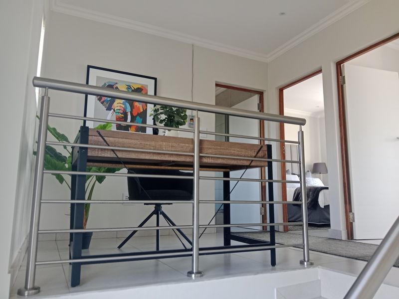 A bright landing area featuring a modern stainless steel balustrade, tiled flooring, and access to adjacent bedrooms.