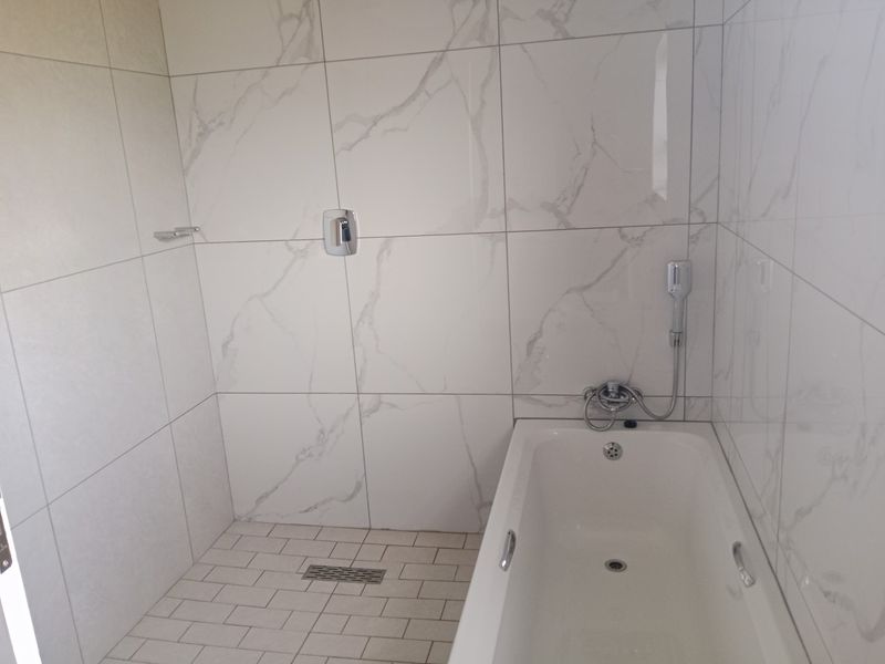 A modern bathroom featuring a built-in bathtub with a handheld shower attachment and elegant marble-look wall tiling.