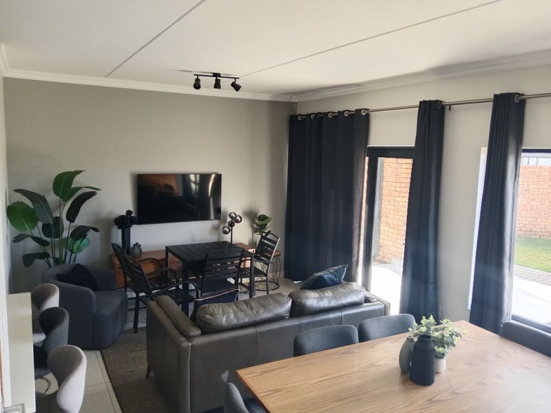 An open-plan living and dining area featuring tiled flooring, track lighting, and direct access to the rear garden through a sliding glass door.