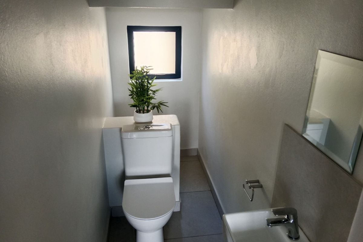 A compact guest bathroom featuring a modern toilet, wall-mounted basin with mixer tap, and tiled flooring.