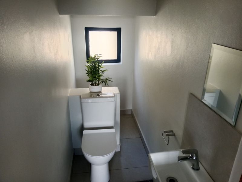 A compact guest bathroom featuring a modern toilet, wall-mounted basin with mixer tap, and tiled flooring.