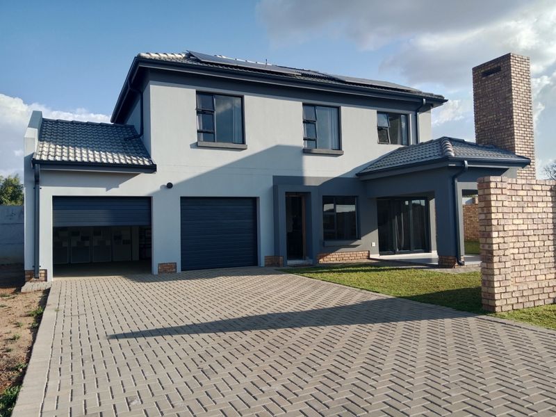 Modern double-storey residential home featuring a paved driveway, double garage, solar panels, and a prominent brick chimney.