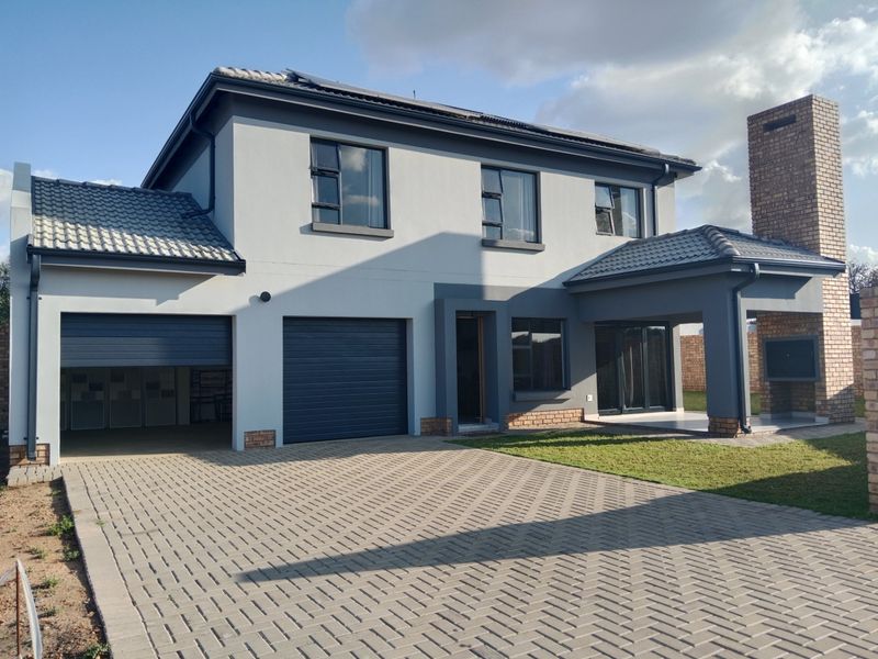 Modern double-story house featuring a paved driveway, double garage, and a covered patio with a built-in braai.