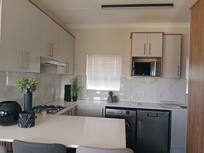 Modern kitchen featuring light-toned cabinetry, quartz countertops, marble-look splashbacks, and integrated appliances including a gas hob and dishwasher.