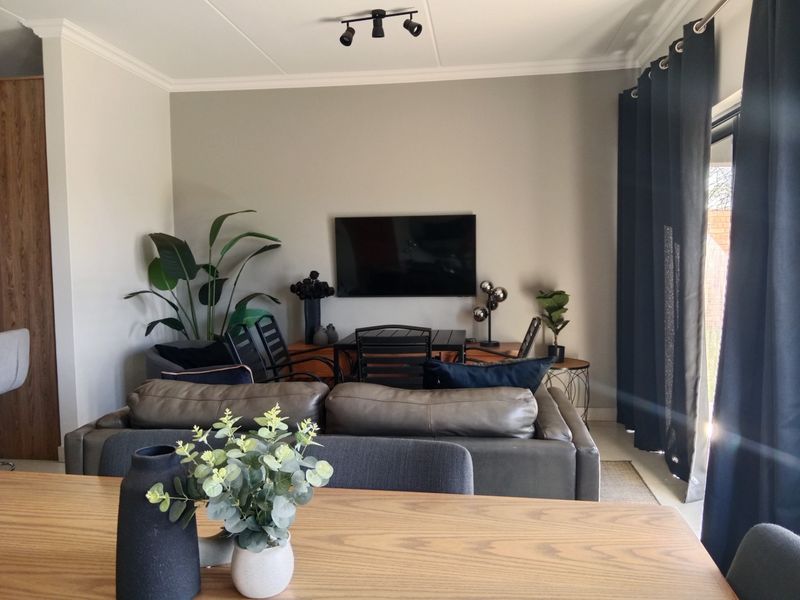 An open-plan living area featuring neutral walls, coving, modern ceiling spotlighting, and a large sliding glass door providing access to the exterior.