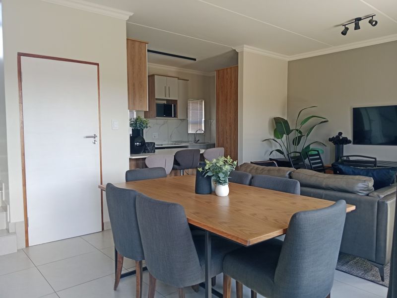 A modern open-plan living and dining area featuring tiled floors, neutral walls, and a functional kitchen with built-in cabinetry and integrated appliances.