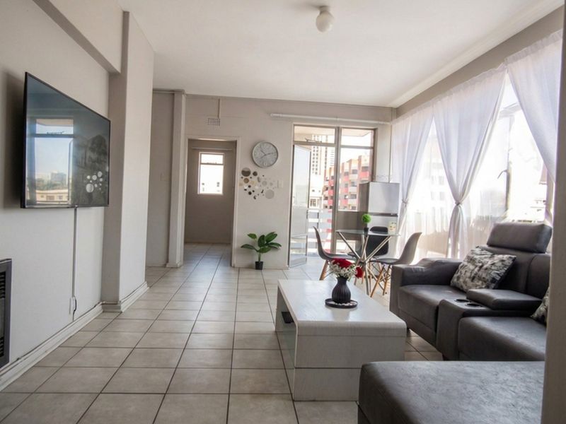 A bright living room featuring neutral tiled flooring, coved ceilings, and a sliding glass door providing access to an outdoor balcony area.