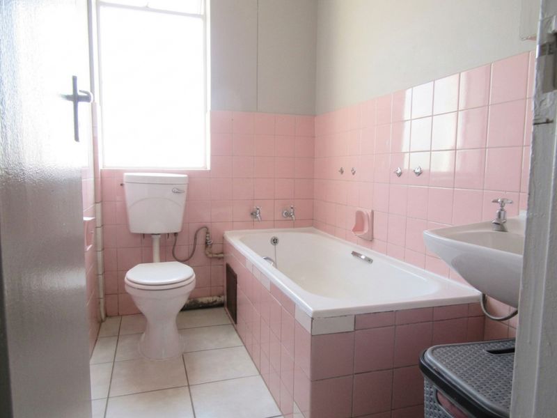 A dated bathroom featuring original pink wall tiles, a standard bathtub, pedestal basin, and toilet, offering significant potential for a modern renovation.