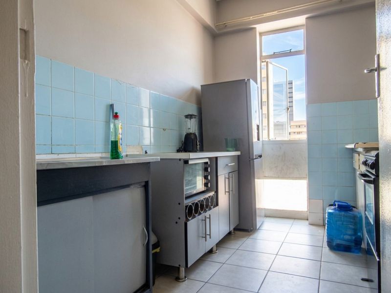 A functional kitchen featuring tiled splashbacks, built-in cabinetry, and tiled flooring, with natural light provided by a large window.