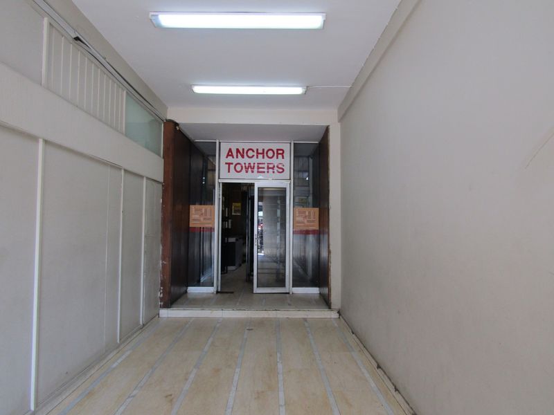 A functional apartment building entrance lobby featuring tiled flooring, fluorescent lighting, and a glass doorway leading into the Anchor Towers complex.