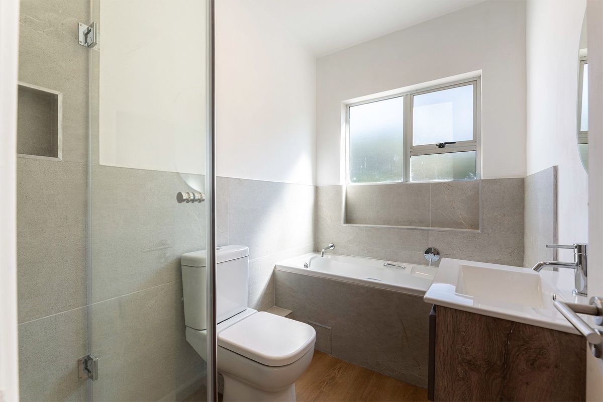 Modern bathroom featuring a glass-enclosed shower, built-in bathtub, vanity with basin, and neutral stone-look wall tiling.