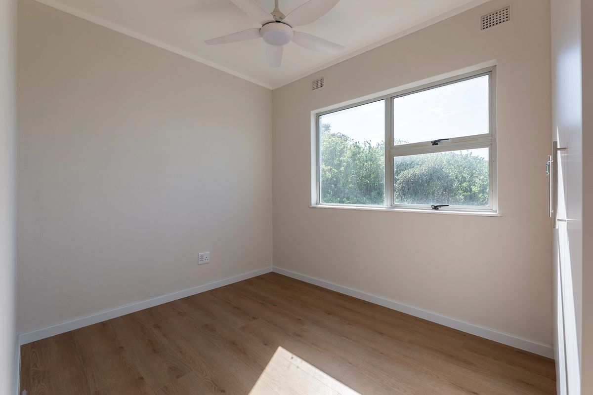 A bright, empty bedroom featuring modern laminate flooring, a ceiling fan, and a built-in cupboard, offering a clean and neutral space.