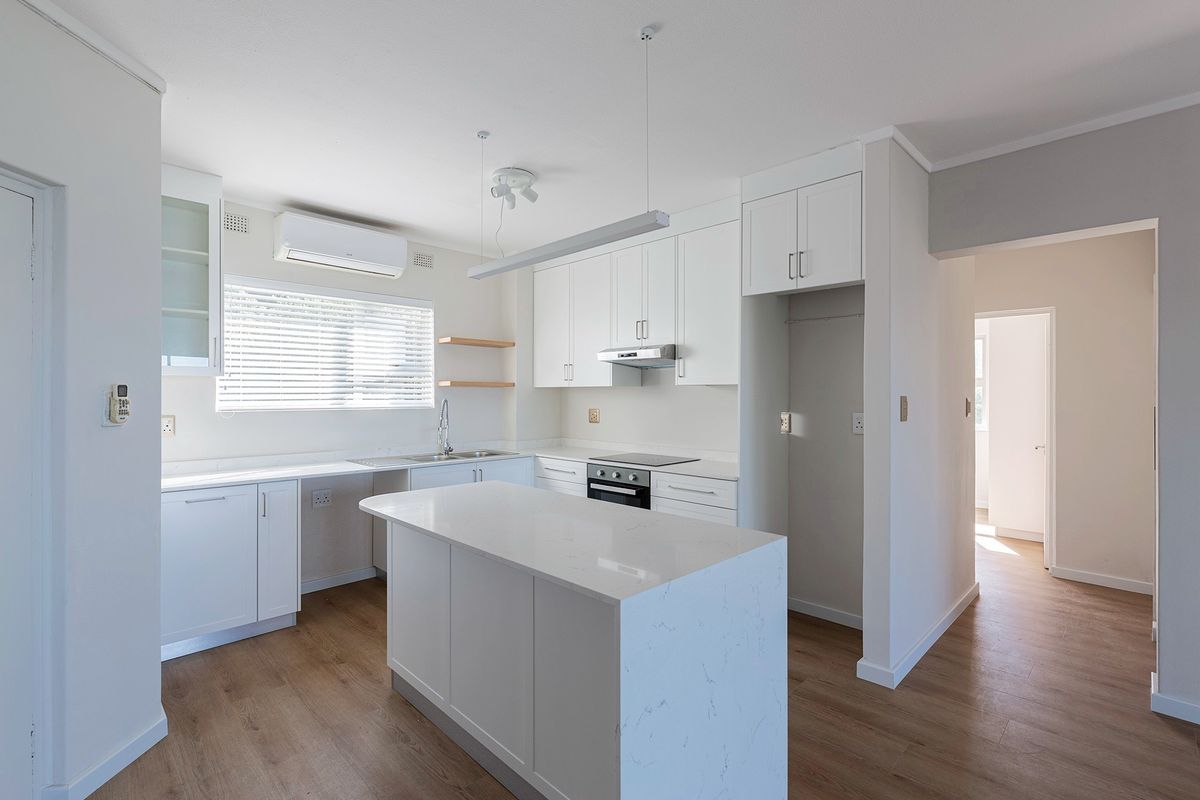 Modern, bright kitchen featuring white shaker-style cabinetry, quartz countertops, a central island, and integrated appliances, finished with light wood-look flooring.