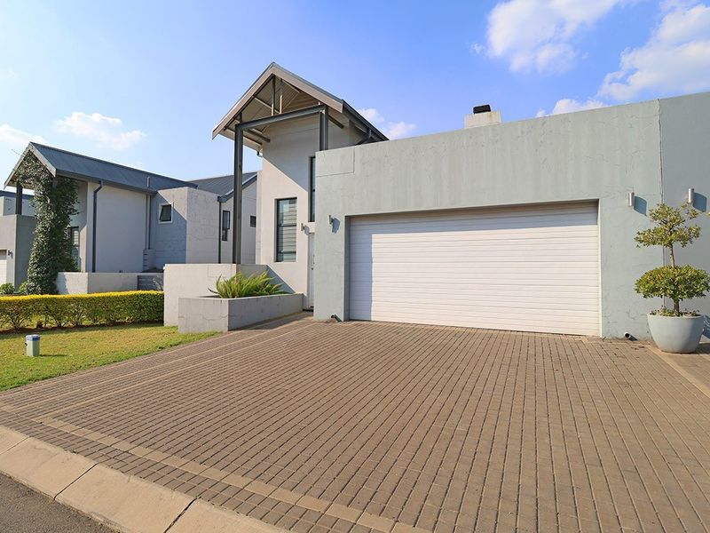 Modern front elevation featuring a paved driveway, automated garage door, and contemporary architectural design with clean lines and well-maintained exterior finishes.