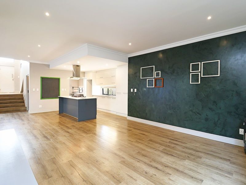 Spacious open-plan living area featuring a modern kitchen with a central island, sleek cabinetry, and durable laminate flooring, leading to an internal staircase.