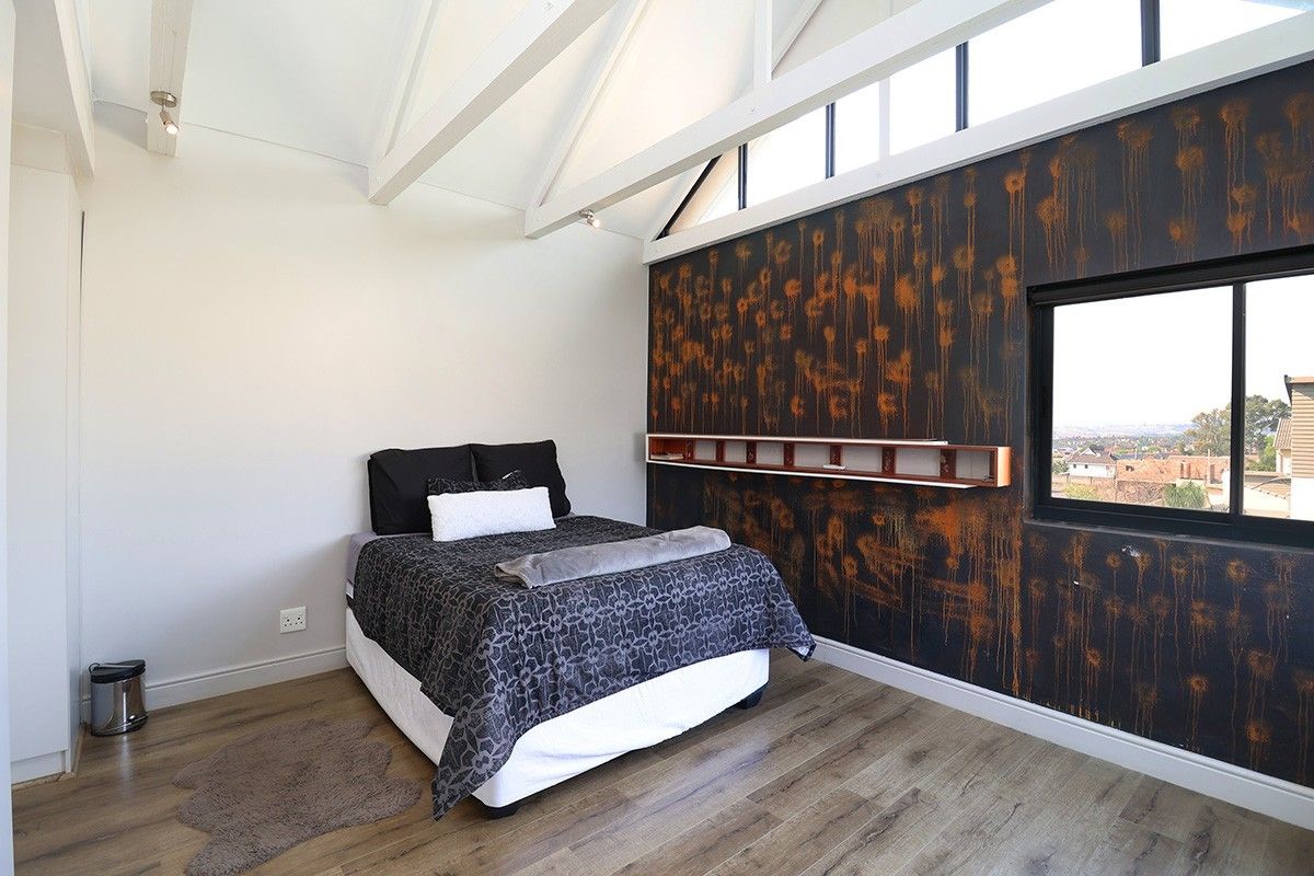 Spacious bedroom featuring high vaulted ceilings with exposed rafters, clerestory windows for natural light, laminate flooring, and a unique decorative feature wall.