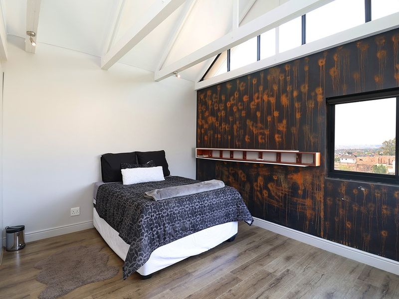 Spacious bedroom featuring high vaulted ceilings with exposed rafters, clerestory windows for natural light, laminate flooring, and a unique decorative feature wall.