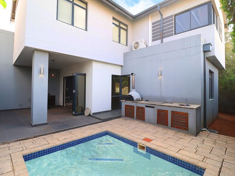 Outdoor entertainment area featuring a swimming pool, built-in braai, pizza oven, and sink, seamlessly connected to the home via bi-fold doors.